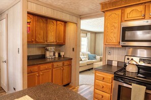 A compact kitchen with wooden cabinets, a microwave, a stove, and a coffee maker.