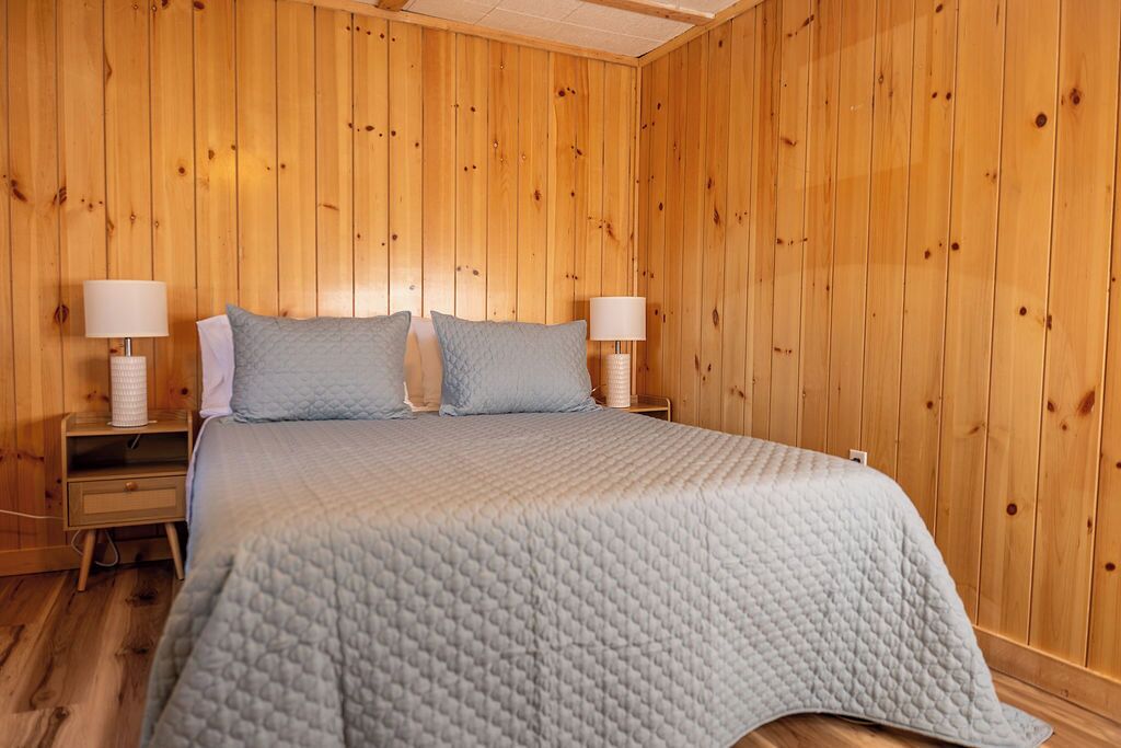 Una stanza con rivestimento in legno, un letto, due lampade da comodino e un comodino.