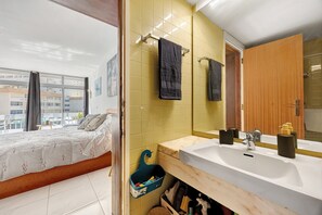 Hotellihuone, jossa on sänky, kylpyhuone, jossa on pesuallas, ja ikkuna, josta on näkymä rakennuksiin.