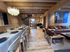 A dining area with a long table set for a meal, a staircase leading to an upper level, and a living area with a sofa and coffee table. - -Les Clématites- Exclusive Chalet in the Heart of Villars-sur-Ollon (Villars-sur-Ollon)