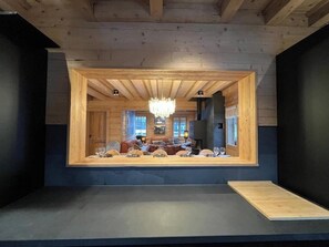 Zona pranzo con soffitto in legno, un lampadario e vista su un soggiorno con camino.