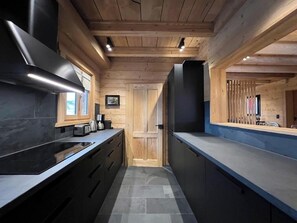 A modern kitchen with wooden beams, a black stove, and a grey countertop. - -Les Clématites- Exclusive Chalet in the Heart of Villars-sur-Ollon (Villars-sur-Ollon)