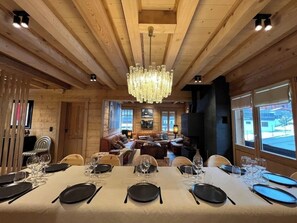 A dining area with a long table set for a meal, a chandelier, and a fireplace in the background. - -Les Clématites- Exclusive chalet in the heart of Villars-sur-Ollon (Villars-sur-Ollon)