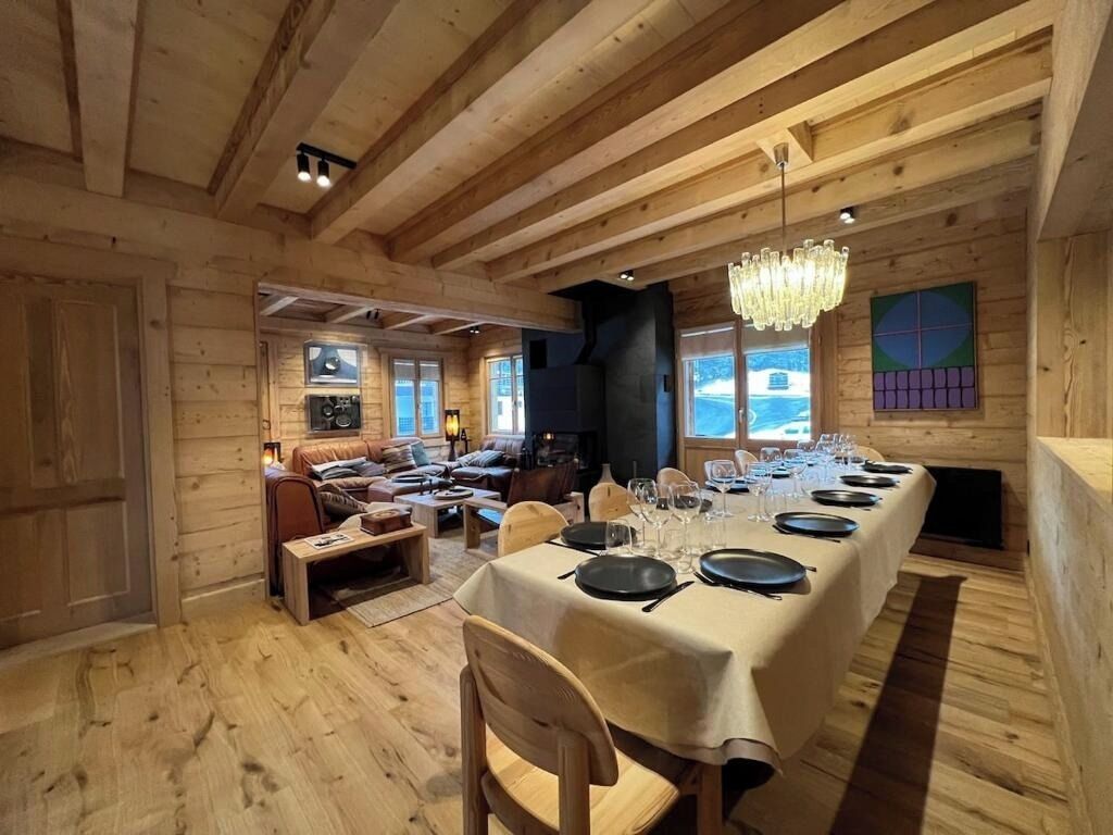 A wooden interior with a long dining table set for a meal, a fireplace, and a cozy seating area.