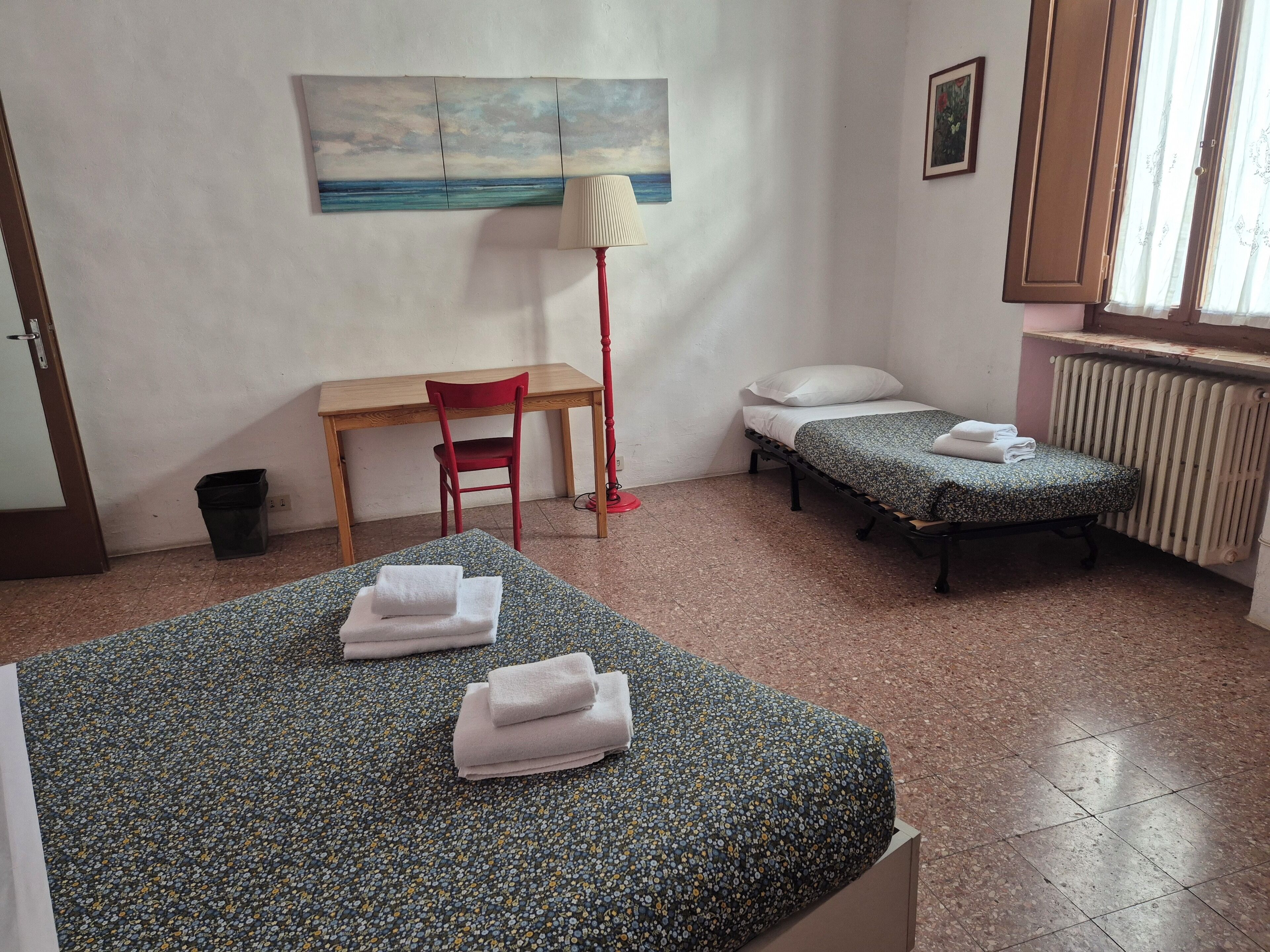 Une chambre avec deux lits simples, un bureau, une chaise, une lampe sur pied et un radiateur.