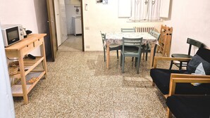 Eine kompakte Küche mit Mikrowelle, kleinem Kühlschrank und Spüle. Ein Esstisch mit Stühlen und einer Bank steht bereit. Der Boden ist mit Fliesen ausgelegt.
