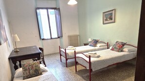 Ein Zimmer mit zwei Betten, einem kleinen Tisch, einem Stuhl und einem Fenster.