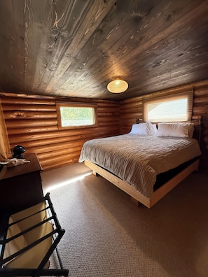 Ein Schlafzimmer in einer Blockhütte mit einem Bett, einem Schreibtisch und einem Stuhl.