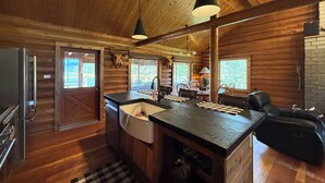 Interior de uma cabana com cozinha, sala de jantar e lareira.