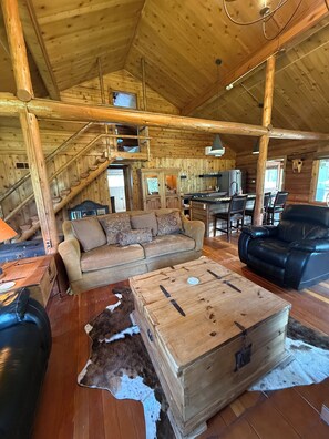 Een rustiek chaletinterieur met een houten trap, een bank, een eettafel en een leren stoel.
