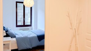 A bedroom with a bed, a window, a radiator, and a hanging light fixture. - Central Geneva Apartment - Walk to Old Town & Lake (Genève)