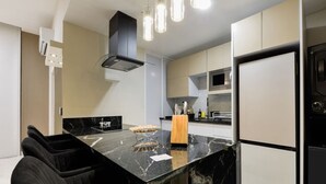 Une cuisine moderne dotée d’un îlot en marbre noir, de tabourets de bar noirs, d’un four encastré et d’un réfrigérateur en acier inoxydable.