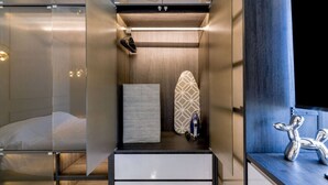 Une chambre d’hôtel moderne et compacte, comprenant un lit, un petit coin salon, une coiffeuse et une douche.