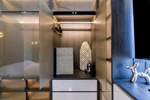 Une chambre d’hôtel moderne et compacte, comprenant un lit, un petit coin salon, une coiffeuse et une douche.