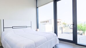Ein modernes Schlafzimmer mit einem großen Bett, Blick auf die Stadt durch eine Schiebeglastür und minimalistischem Design.