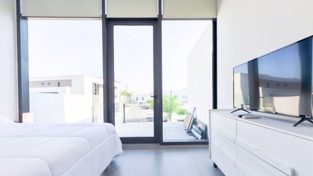 Ein modernes Schlafzimmer mit einem großen Bett, einem Fernseher auf einer Kommode und einer Glastür zum Balkon.