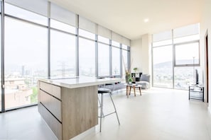 Eine moderne Küche mit einer großen Kochinsel, Barhocker und Blick auf die Stadt durch große Fenster.