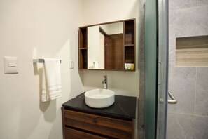 Ein Badezimmer mit einem runden Waschbecken, einem Holz-Waschtisch, einem Spiegel und einem Handtuchhalter.