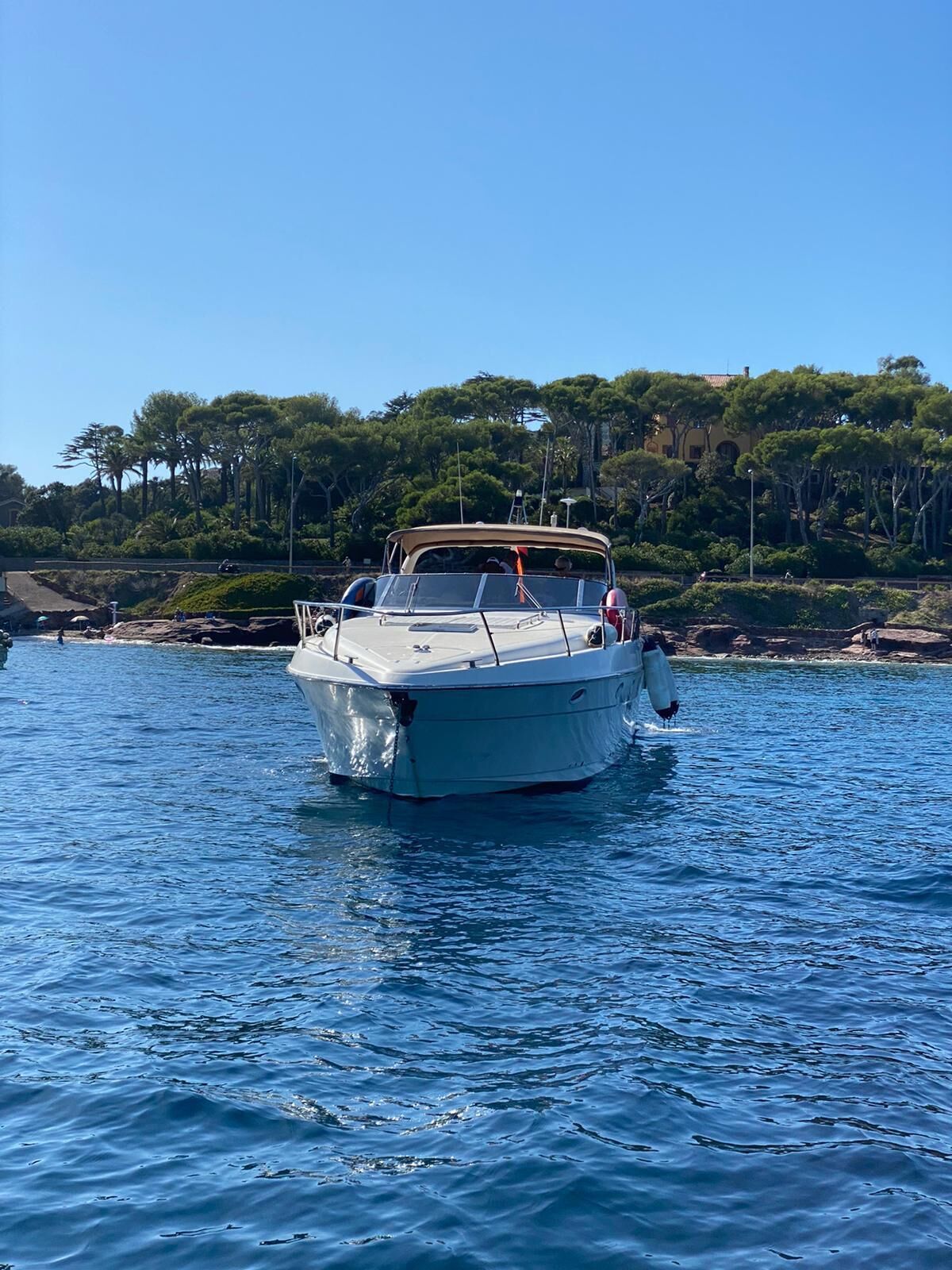 Un bateau sur une mer calme, avec une côte rocheuse et des arbres en arrière-plan.