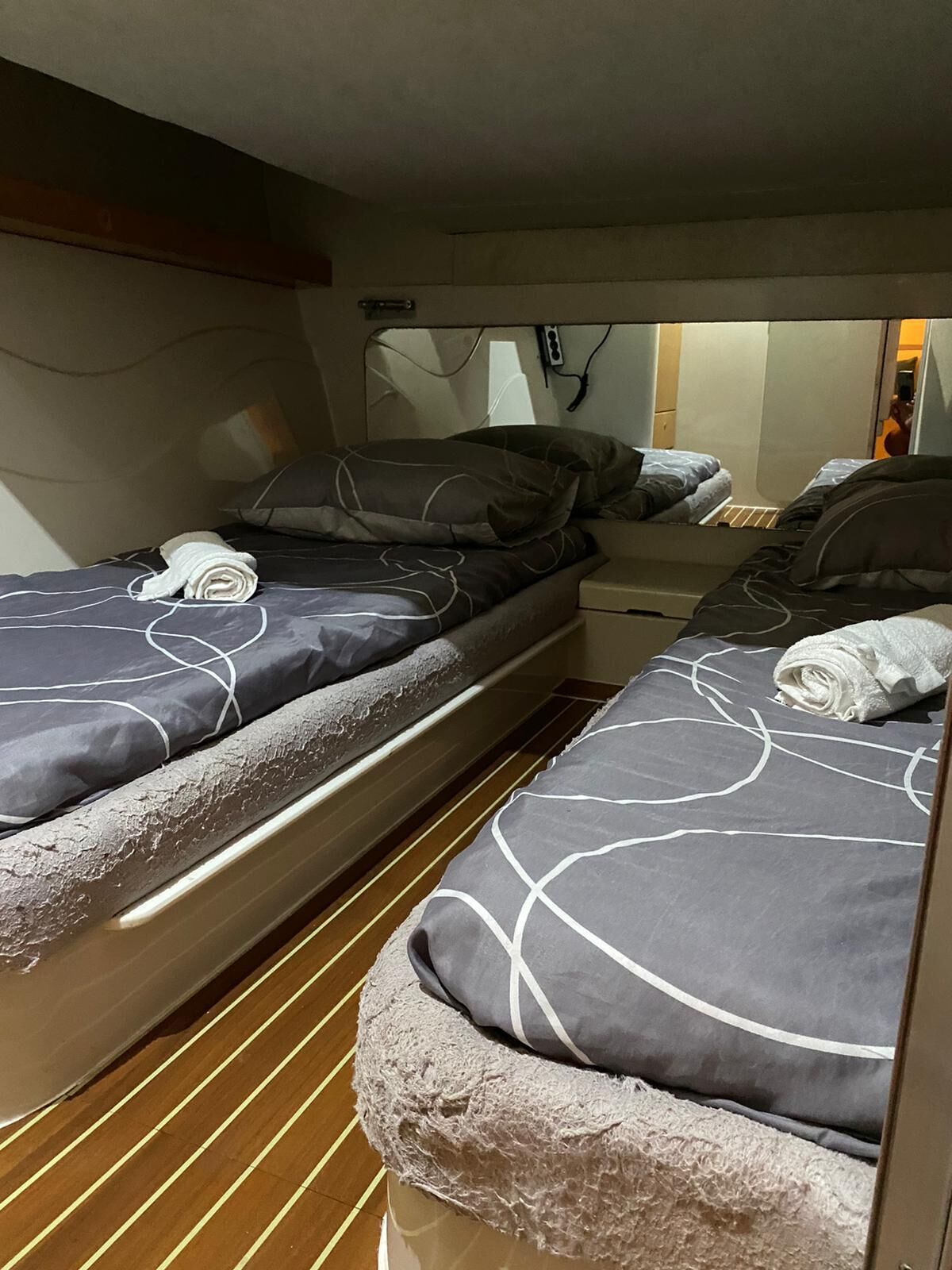 A compact cabin with two beds, each with a grey and white patterned bedspread, and a wooden floor.