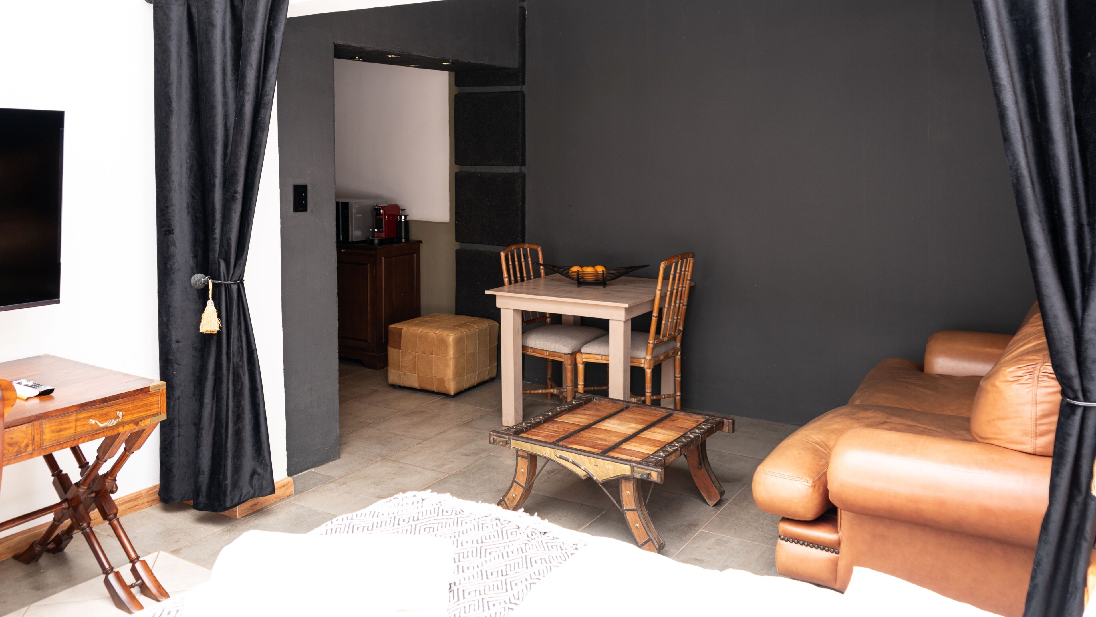 Un espacio habitable funcional con un sofá, una mesa de comedor con sillas, un pequeño armario de madera y un televisor.