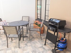 An outdoor patio with a round table, chairs, a grill, and a flower planter. - The Lombard Manor (Pretoria)