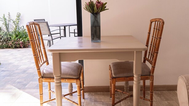 Una mesa de comedor con dos sillas, un florero con flores y vista al exterior.