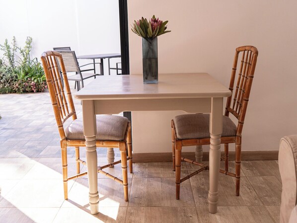 A dining table with two chairs, a vase with flowers, and a view of the outdoors.