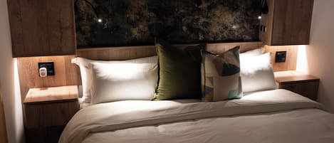 A bed with a white mattress and pillows, wooden headboard, and nightstands with a power outlet.