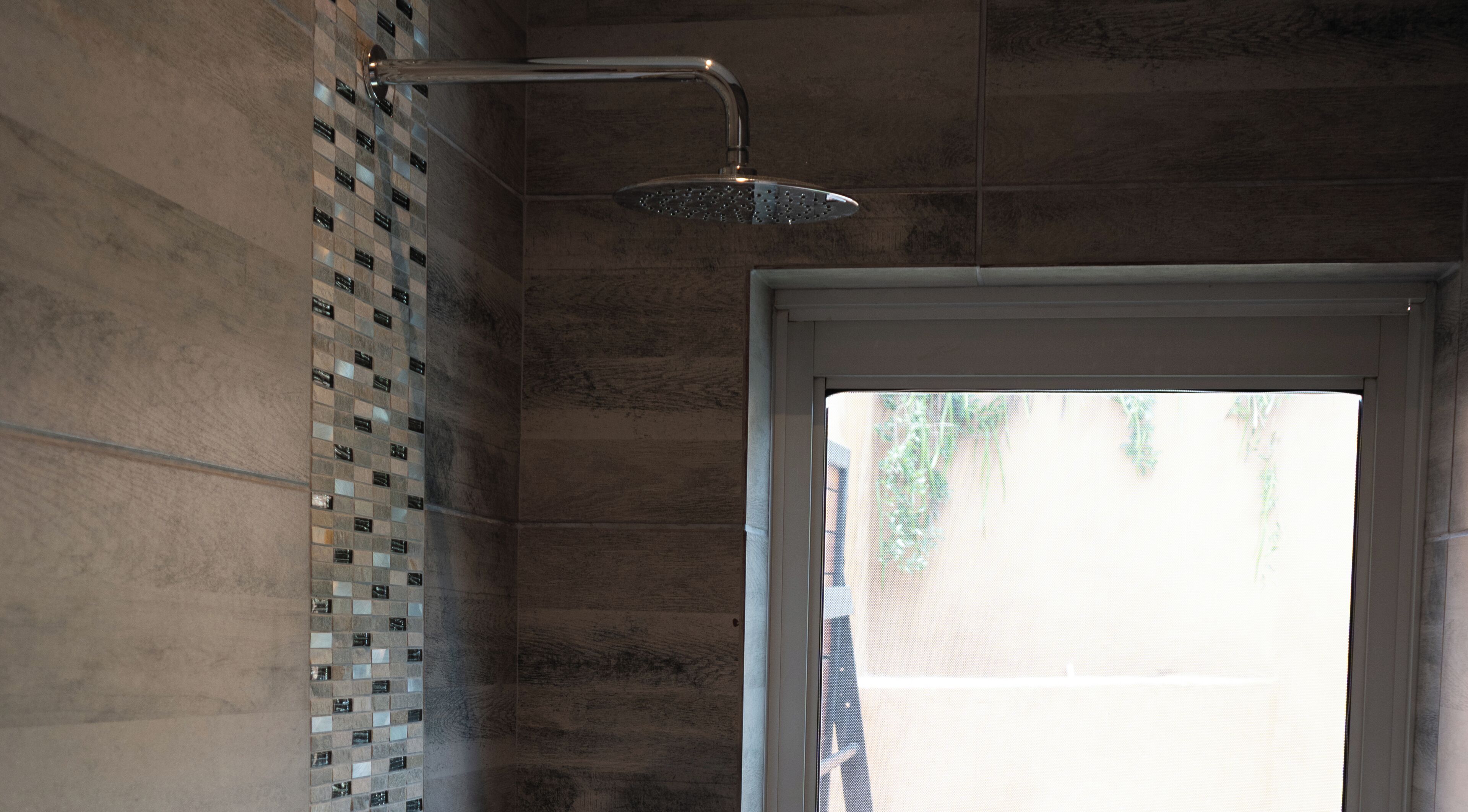 A shower with a rain showerhead and a tiled wall.