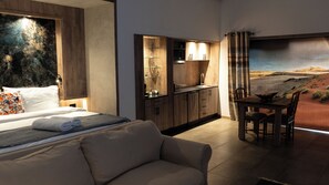 A modern hotel room with a bed, a dining area, and a view of a desert landscape.