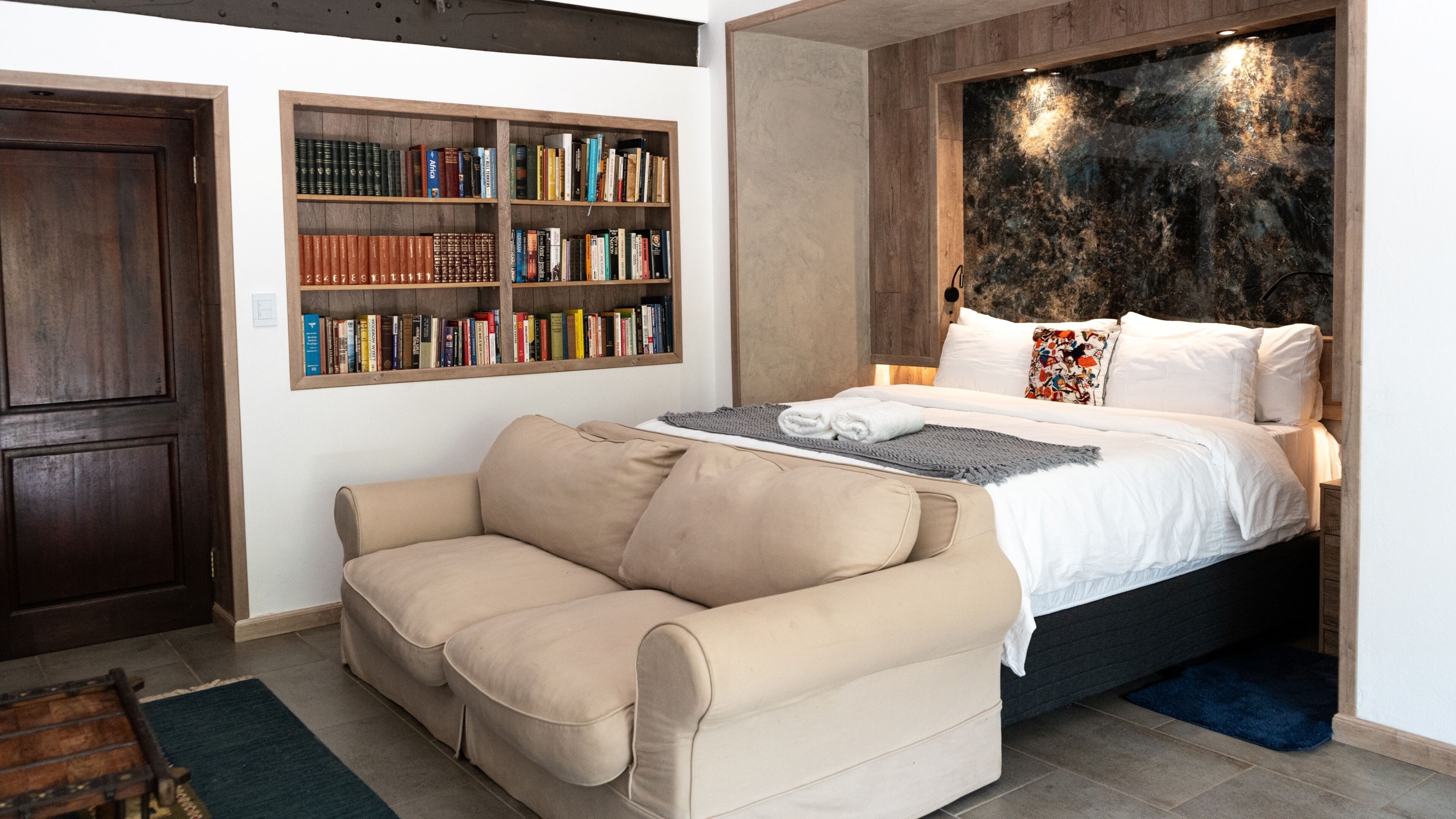 Ein Schlafzimmer mit einem Bett, einer Couch, einem Bücherregal und einer Marmorwand.