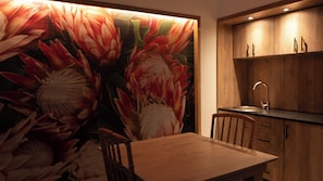 Un área de comedor con una mesa y sillas, una pared con un mural floral y armarios de madera con un lavabo.