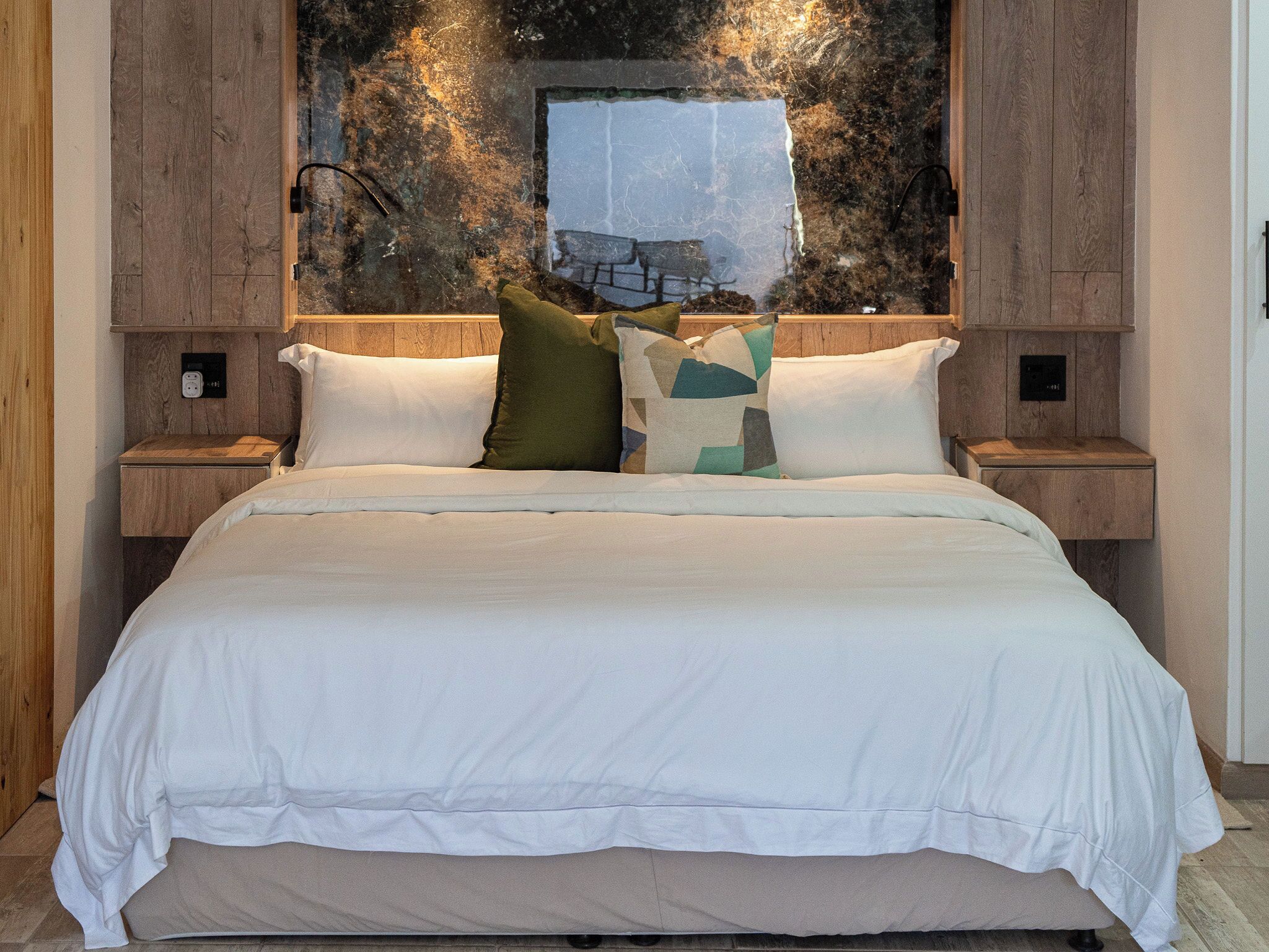 A bedroom with a large bed, two bedside tables, and a wall-mounted light fixture.