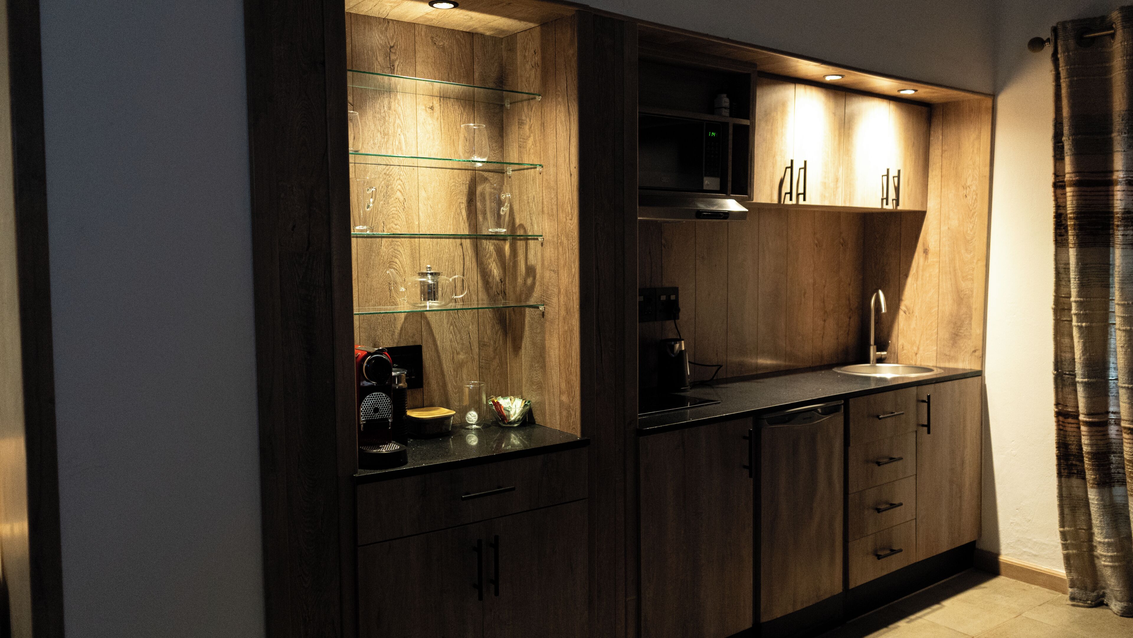 Een moderne keuken met houten kastjes, een glazen plank en een koffieapparaat.