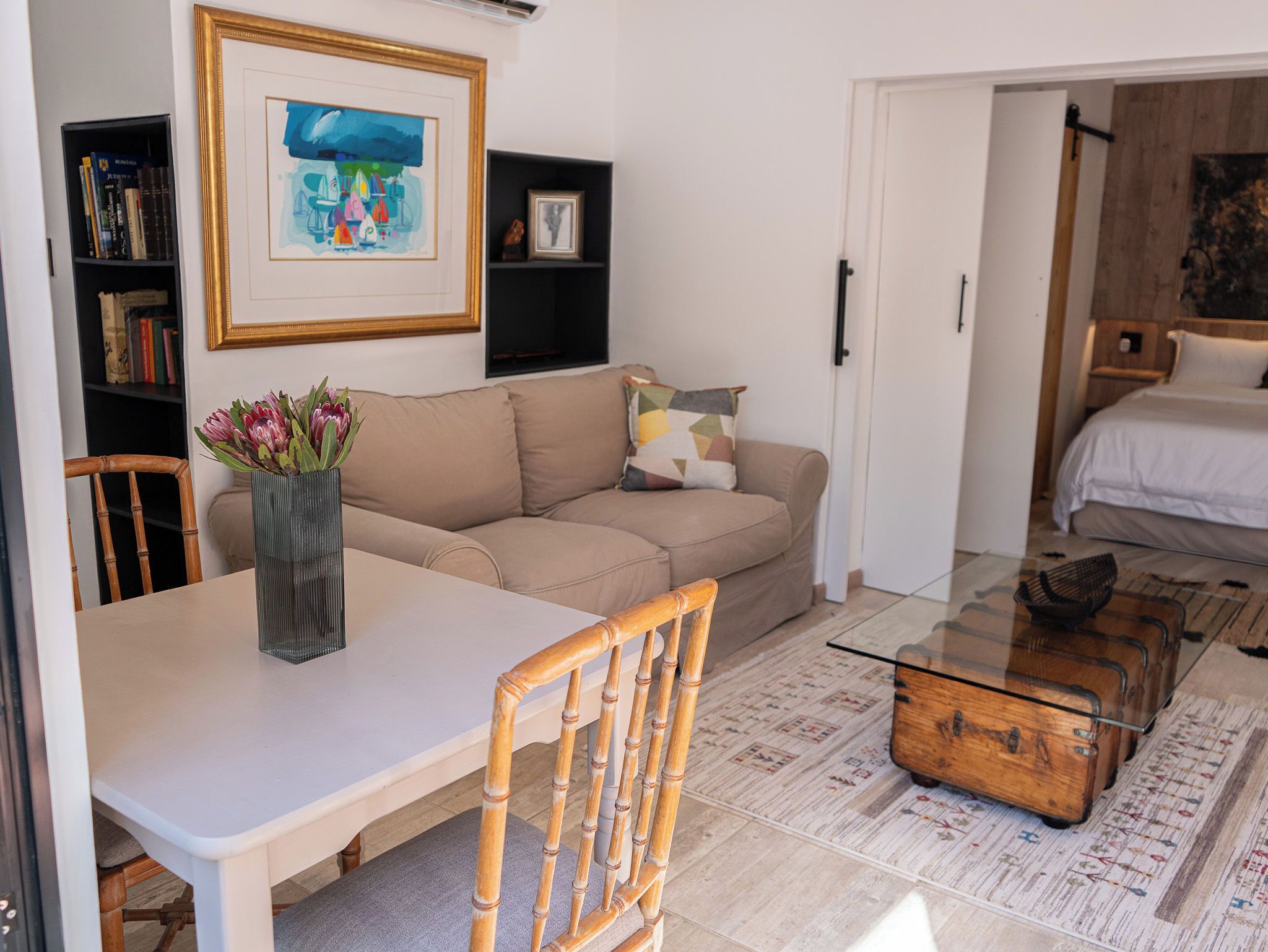 A living room with a sofa, a coffee table, a bookshelf, and a painting on the wall.