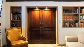 Una habitación con un gran puerta doble de madera, dos estanterías a cada lado y un sillón de cuero.