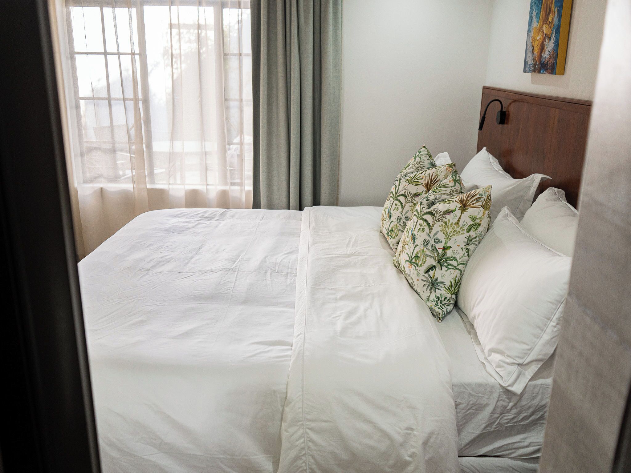 Una habitación de hotel con cama, ventana con cortinas y un cuadro en la pared.