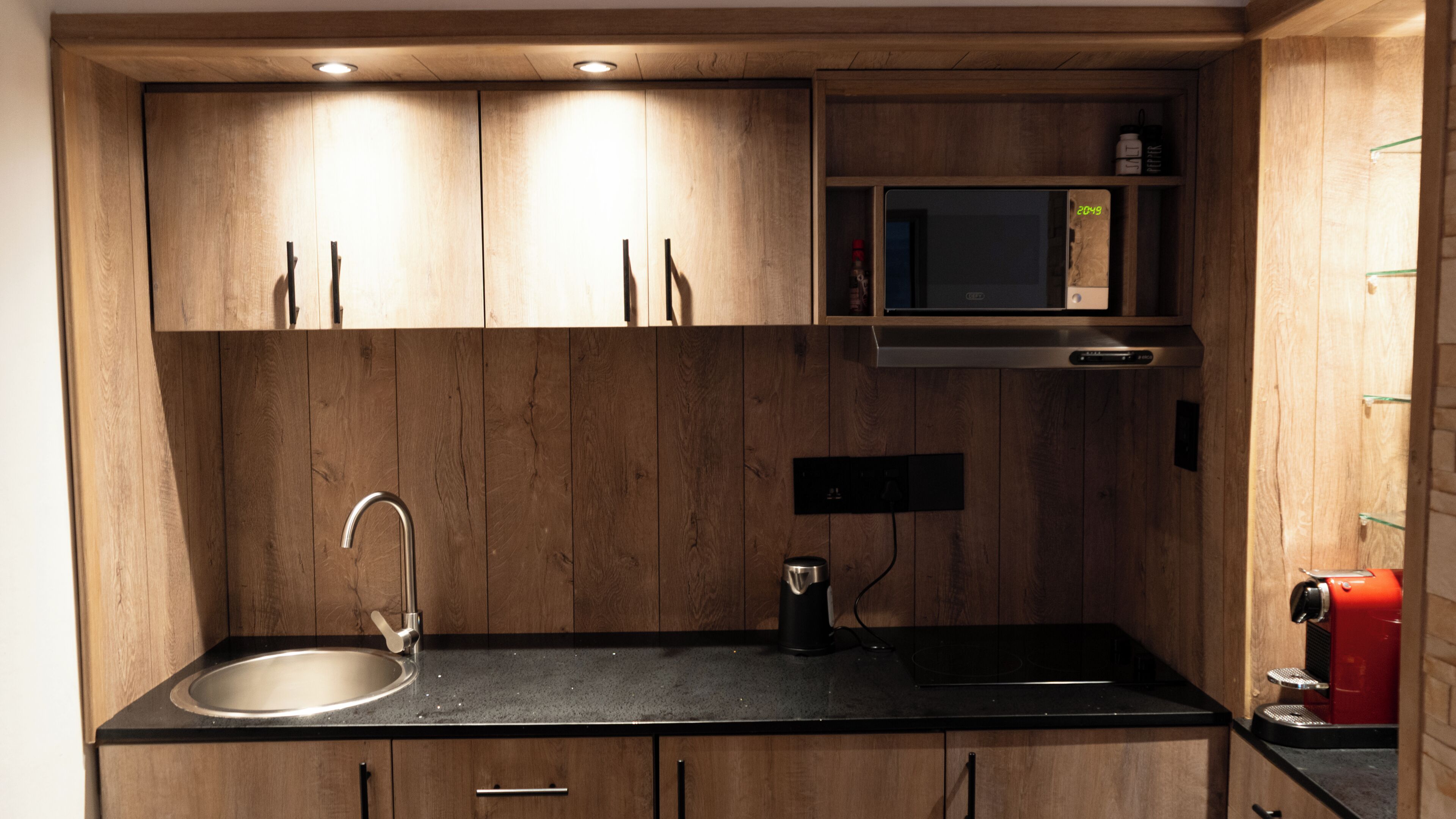 A kitchen with wooden cabinets, a stainless steel sink, a microwave, and a red coffee machine.