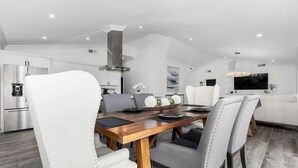 Una cocina moderna con electrodomésticos de acero inoxidable, un comedor con mesa de madera y sillas tapizadas, y una sala de estar con sofá y televisor de pantalla plana.