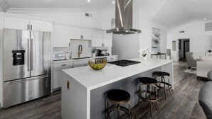 Una cocina moderna con electrodomésticos de acero inoxidable, una isla central con taburetes y una encimera de mármol gris.