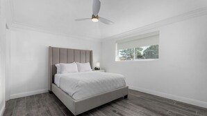 Un dormitorio con cama, ventilador de techo, mesita de noche y ventana.