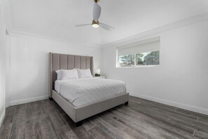Ein Schlafzimmer mit Bett, Deckenventilator, Nachttisch und Fenster.