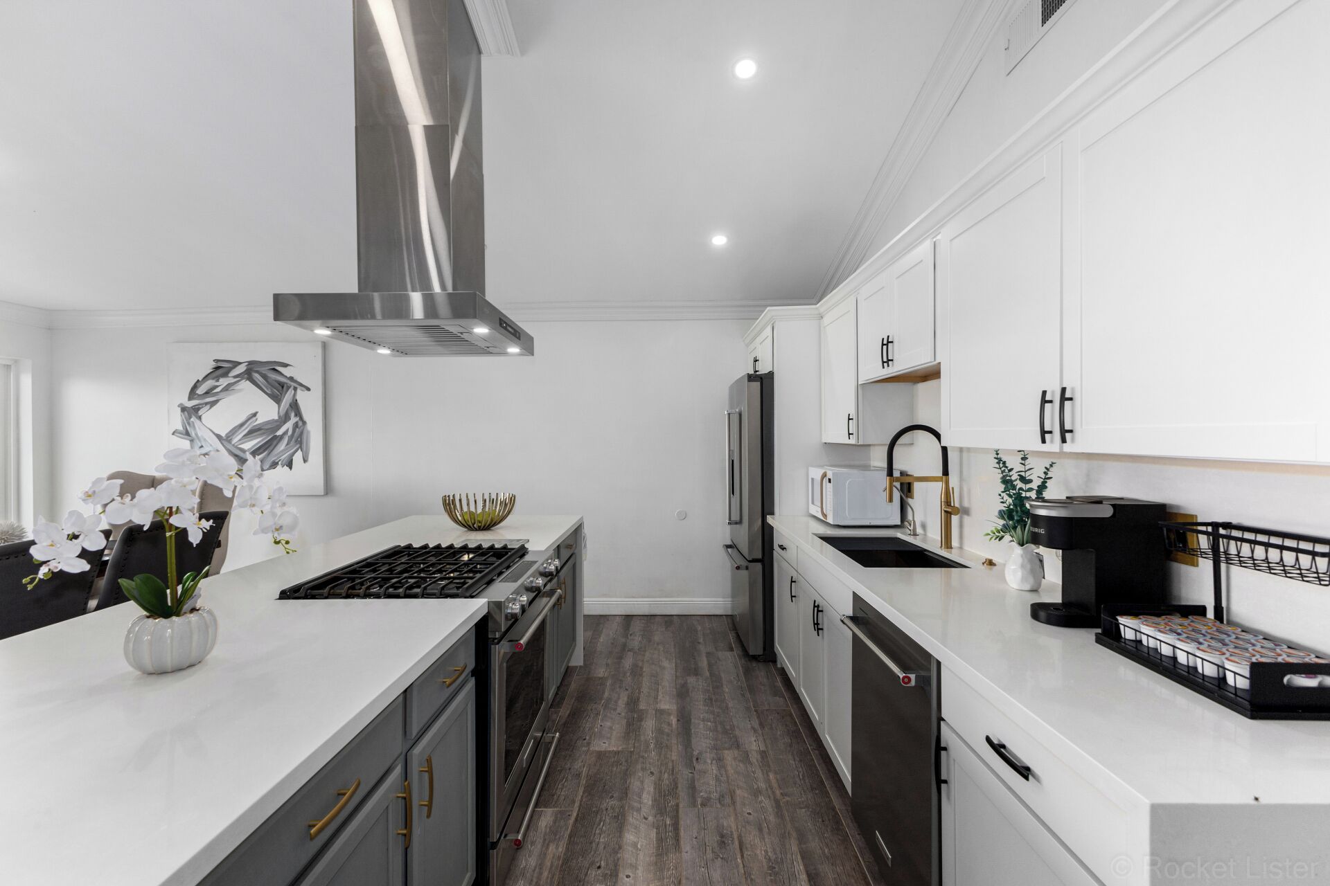 A modern kitchen with white cabinetry, stainless steel appliances, and a wooden floor.