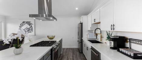 A modern kitchen with white cabinetry, stainless steel appliances, and a wooden floor.