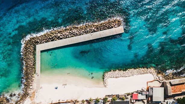 An aerial view of a coastal area with a beach, a rocky breakwater, and buildings in the foreground. - Majestic 1-Bed Balcony City View Suite by Bocobay (Willemstad)