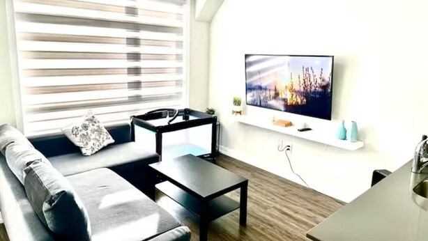 A modern living room with a sofa, coffee table, and a flat-screen TV mounted on the wall. - Modern 3 bed, 2 bath townhouse. (Vaughan)
