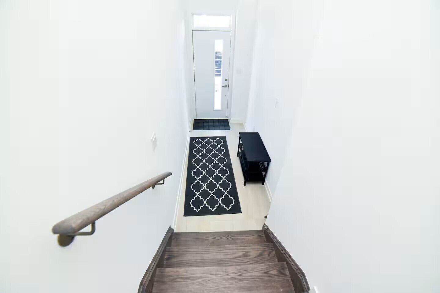 En smal trappa med ett ledstång, en svart, mönstrad matta och en svart bänk längst ner.