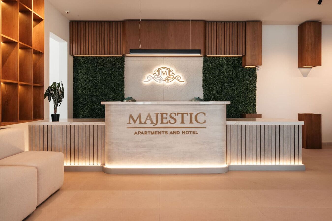 Vastaanottotiski, jossa on kyltti, jossa lukee ”MAJESTIC APARTMENTS AND HOTEL”, puupanelointi, vihreä seinä ja ruukussa oleva kasvi.