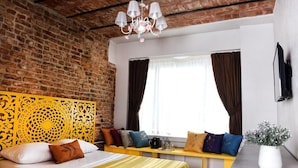 Een hotelkamer met een bakstenen muur, een geel bed, een bank met kussens, een kroonluchter en een raam met gordijnen.